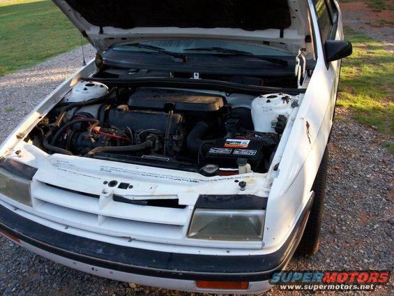 White 1990 Dodge Shadow engine bay with hood open, showing engine, battery, and front grille