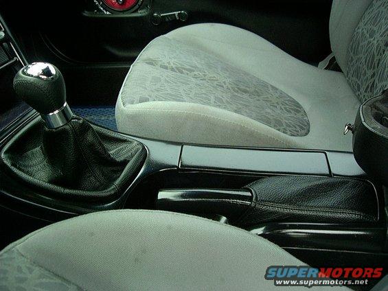 Car interior showing a manual gear shifter, handbrake, and patterned seats. Supermotors.net logo visible