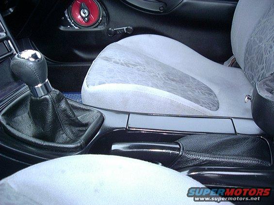 Car interior shot showing gear shifter, handbrake, and part of a seat. Watermark says SUPERMOTORS