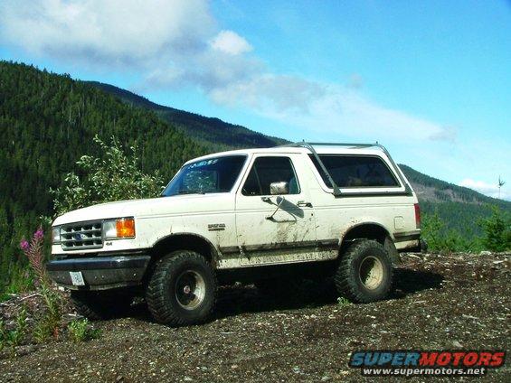 White Ford Bronco parked on a dirt road with a wooded hillside behind it