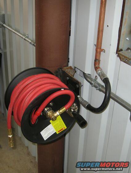 Red air hose on a reel mounted to a brown pipe