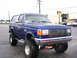 1989 Ford Bronco - A lifted blue Ford Bronco is parked on a wet asphalt lot in front of a commercial building.
