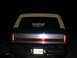 1989 Ford Bronco - Rear view of a 1989 Ford Bronco, a blue body with a silver and red stripe and a tan camper shell.