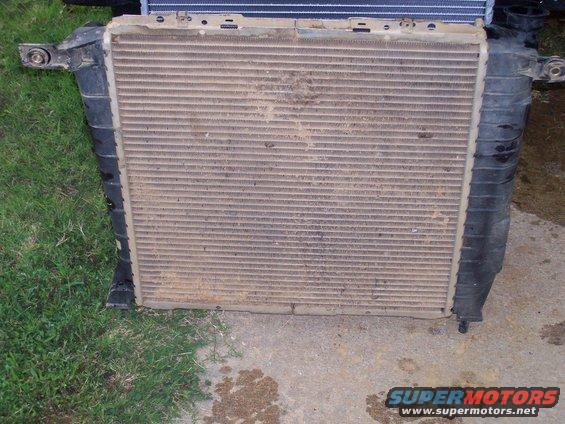 Dirty car radiator with black plastic side tanks, mounted on concrete and grass
