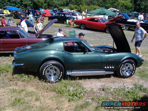 Green 1969 Corvette Stingray parked at car show, hood open. Other cars and people around