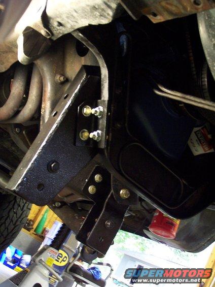 Close-up of black metal lift kit brackets bolted to vehicle frame, with suspension components visible