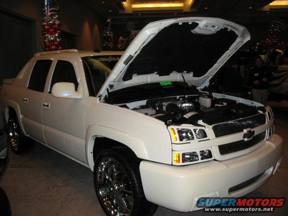 White Chevrolet Avalanche with hood open, showing the engine. Chrome wheels and custom grille