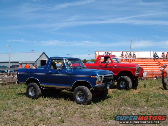 Blue 1978 Ford Bronco parked on grass, side profile visible, with a red Bronco behind it