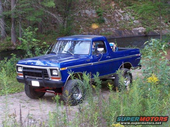 Blue Ford Bronco with lifted suspension parked on a dirt path near a stream