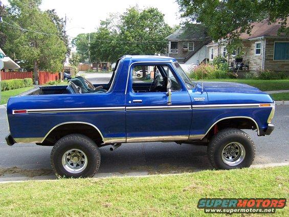 Blue 1979 Ford Bronco parked on street, side view. Has a child seat in the back
