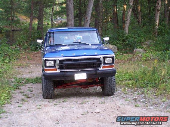 Blue 1979 Ford Bronco parked on a dirt road with trees and a stream in the background