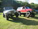 2002 Jeep Wrangler - Two modified off-road vehicles, a Jeep Wrangler and a Ford Bronco, are positioned on a grassy area with logs under their tires.
