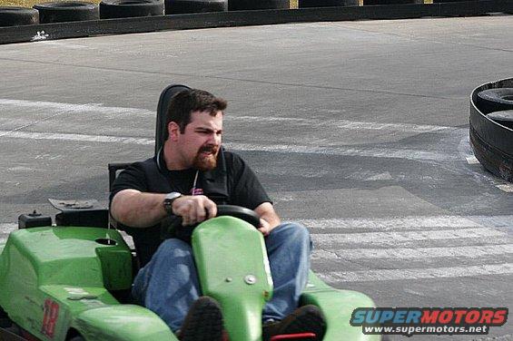 Man driving a green go-kart on a track with tire barriers