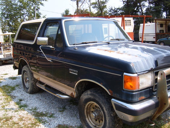 Dark blue and tan Ford Bronco with a white roof, showing rust on the hood and fender