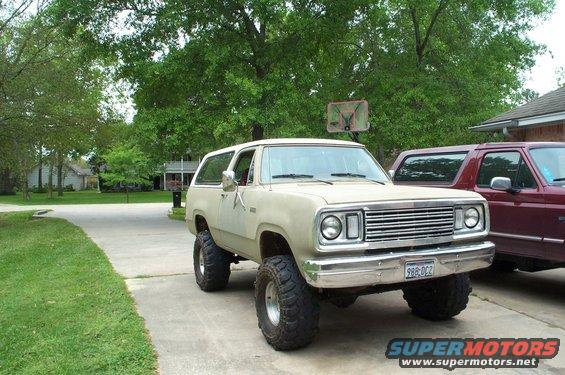 Tan 1978 Dodge Power Ram SUV with large tires parked next to a red pickup truck