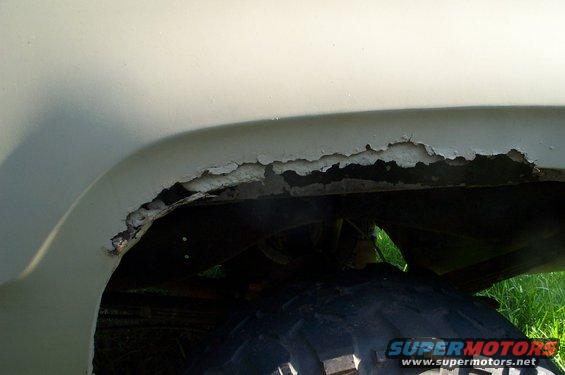 Close-up of rusted metal on a vehicle's wheel well, showing peeling paint and corrosion