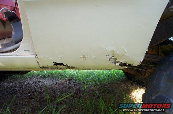 Cream colored truck rocker panel with significant rust and holes, showing the underside and a tire