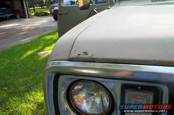 Close-up of a truck's hood and headlight. Another truck is visible in the background