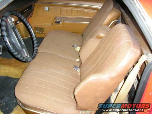 Brown fabric bench seat and dashboard in a car interior. A black steering wheel is visible