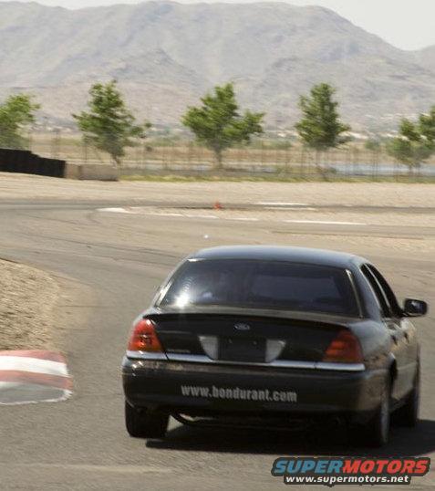 1999 Ford Crown Victoria on a race track, rear view. Website www.bondurant.com visible on trunk lid