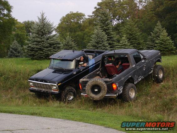 Two black Ford Broncos parked on a grassy hill. One has a blue stripe on its side