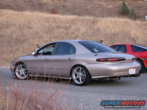 tan sedan parked on roadside, red sports car behind it