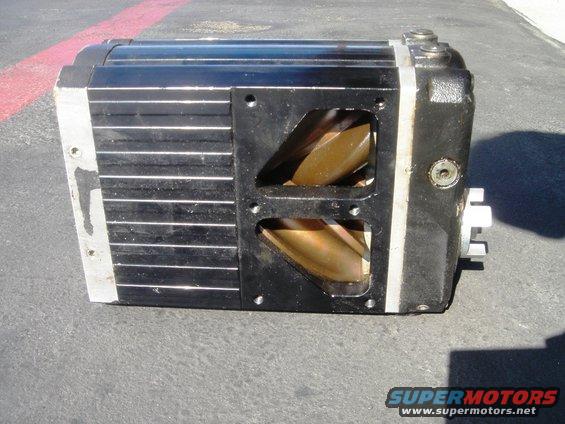 Black supercharger with silver fins and exposed gold rotors, resting on asphalt