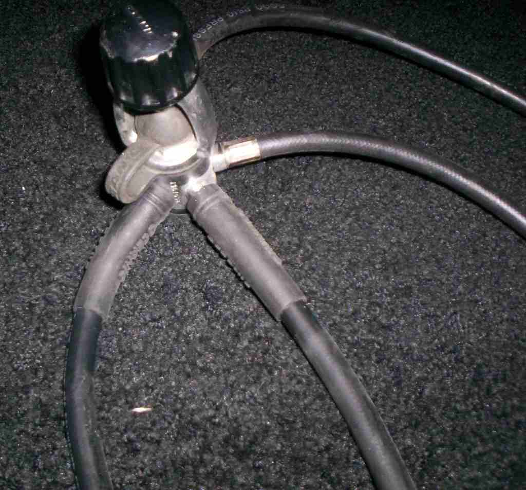 Gas regulator with black knob and three black hoses connected to a metal fitting