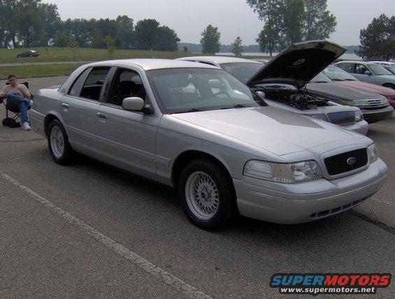 Silver 2002 Ford Crown Victoria parked in a lot with other cars. A person sits in a chair nearby