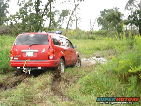 Red SUV stuck in a muddy field with trees in the background
