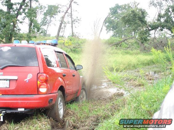 Red SUV with blue lights driving through mud, rear view