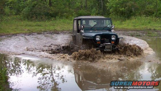 Jeep Wrangler driving through a mud puddle, splashing water and mud
