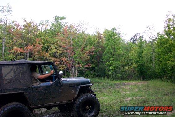 Muddy Jeep CJ-5 driving off-road with trees in the background