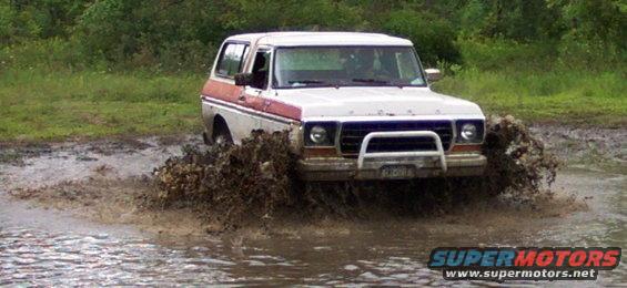 White and red Ford Bronco driving through mud, front bull bar visible