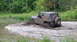 1979 Ford Bronco - A Jeep CJ-7 navigates a muddy water obstacle, kicking up a large spray.