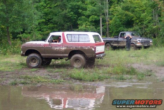 Muddy red and white 1979 Ford Bronco in off-road terrain