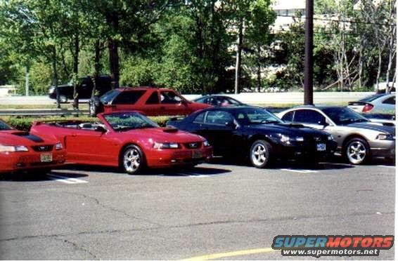 Red convertible Mustang parked in a lot with other cars. License plate is visible