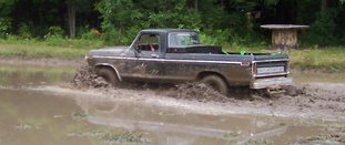 Black Ford pickup truck driving through mud, tires deep in the muck