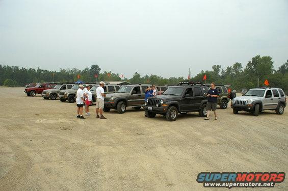 Black Jeep Liberty SUV with roof rack parked on dirt lot, front 3/4 view
