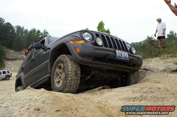 Dark gray Jeep Liberty off-roading on a sandy incline, front-left wheel stuck in a rut