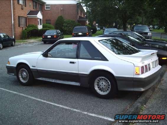 White 1987 Ford Mustang coupe parked in a lot, showing its side profile and rear quarter panel
