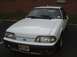 1989 Ford Mustang - A white 1989 Ford Mustang GT is parked in a lot, showing its front end and license plate.