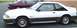 1989 Ford Mustang - A white coupe with dark gray trim and a rear spoiler is parked next to a maroon sedan.