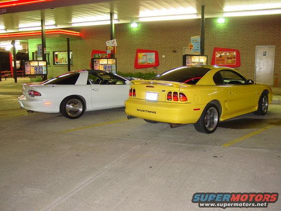 Yellow 1998 Ford Mustang and white Chevrolet Camaro parked at a drive-thru restaurant