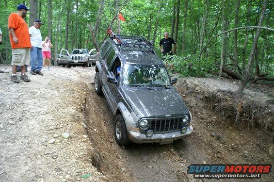 Jeep Liberty going down a muddy trail with people watching. Another Jeep is parked behind it