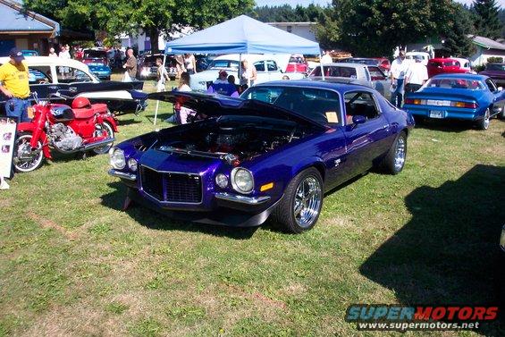 Purple 1970 Chevrolet Camaro with hood open, parked on grass at an outdoor car show. Chrome wheels and custom paint