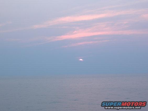 Ocean and sky with pink clouds at sunset, SUPERMOTORS.NET watermark