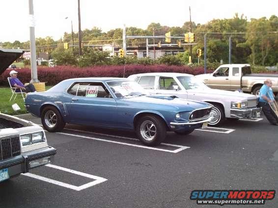 Blue 1969 Ford Mustang parked, with a 'For Sale' sign in the window