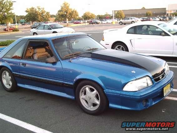 Blue 1989 Ford Mustang coupe with black hood scoop, parked in a lot next to a white car