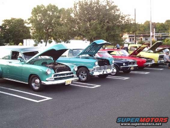 Green panel van with hood open, parked in a lot next to other classic cars